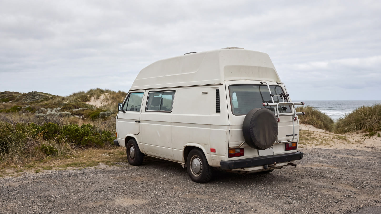 Camper van in a generic coastal reserve beside a blank marker and abstract observation tablet at blue hour