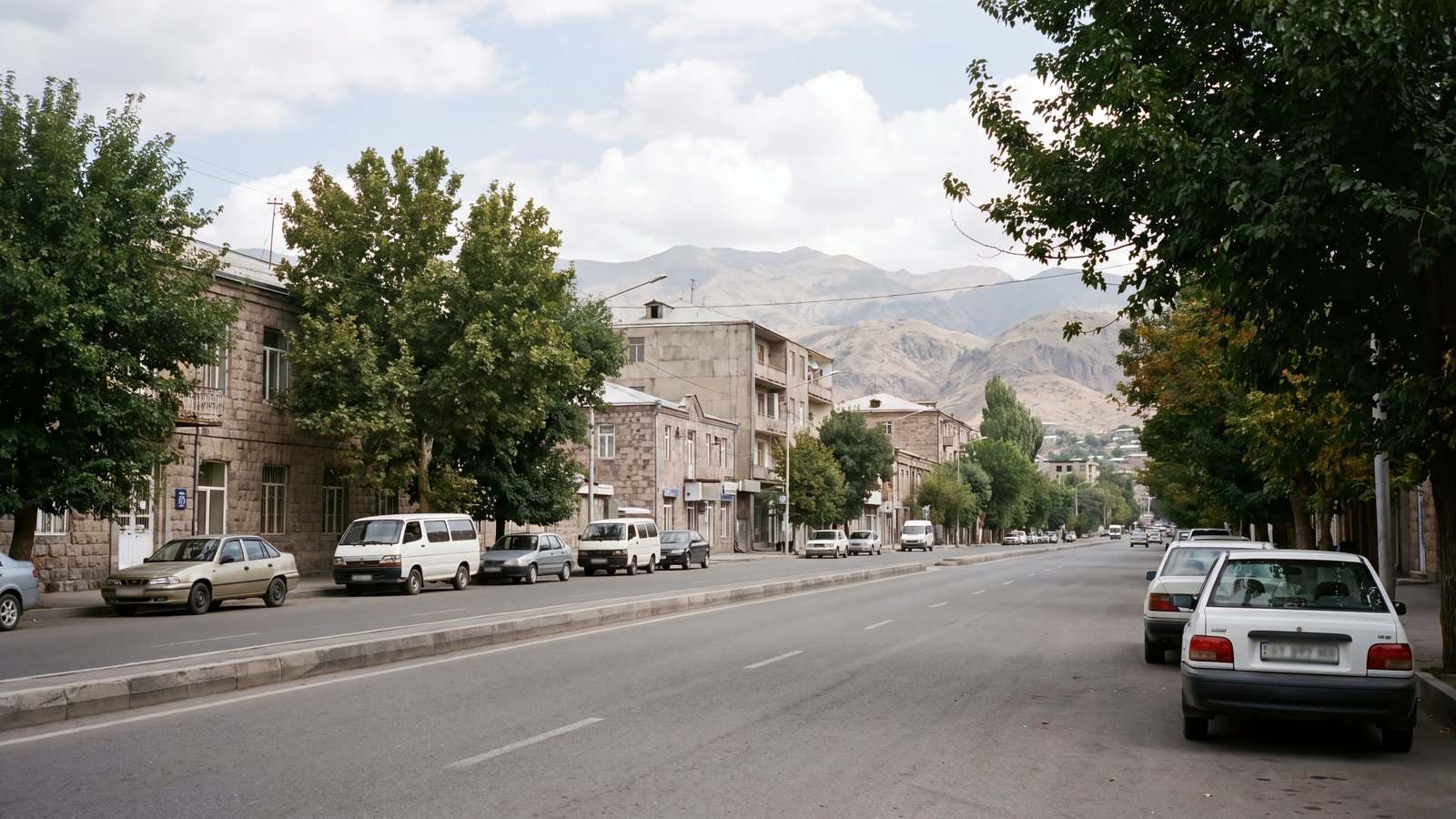 Mountain-edge city parking street with kerbside vehicles and distant hills