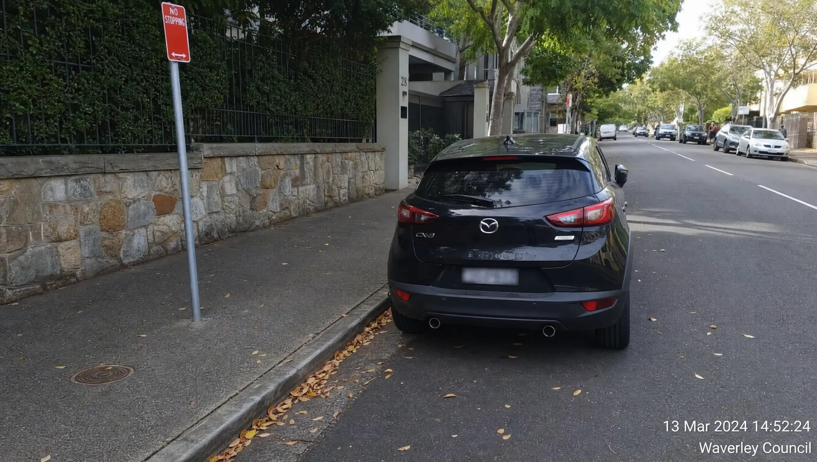Vehicle stopped beside a no-stopping kerb with sign and street context visible